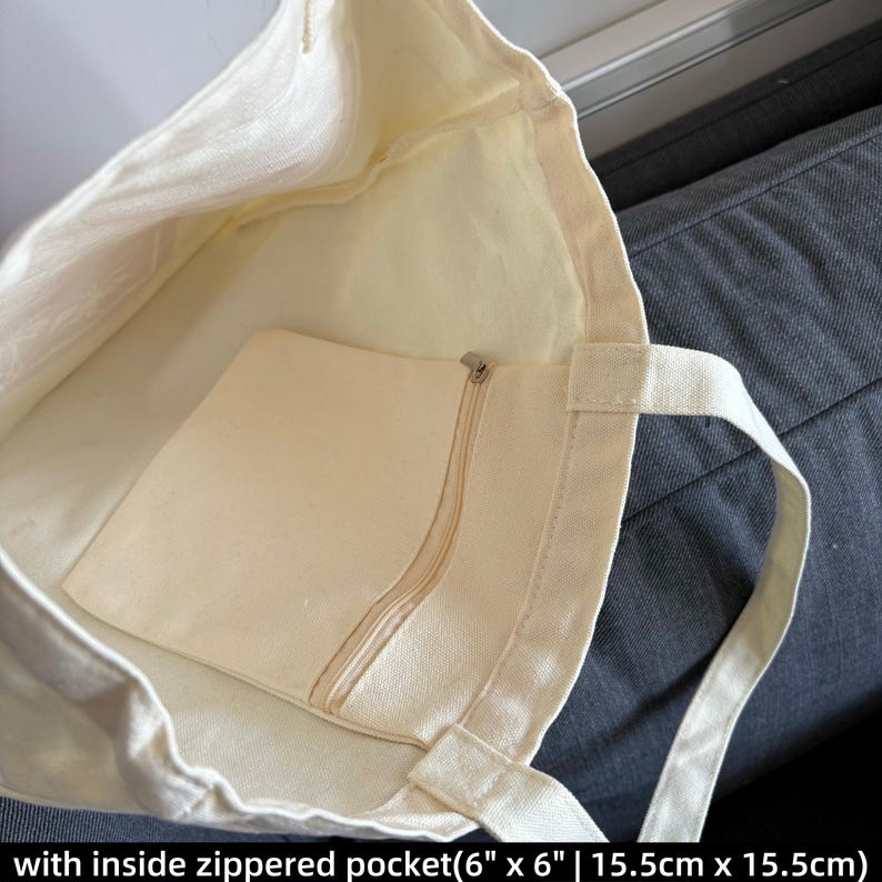 May include: Cream-colored canvas tote bag with an inside zippered pocket. The pocket measures 6 inches by 6 inches. The bag has a simple design with sturdy handles, perfect for carrying everyday essentials.