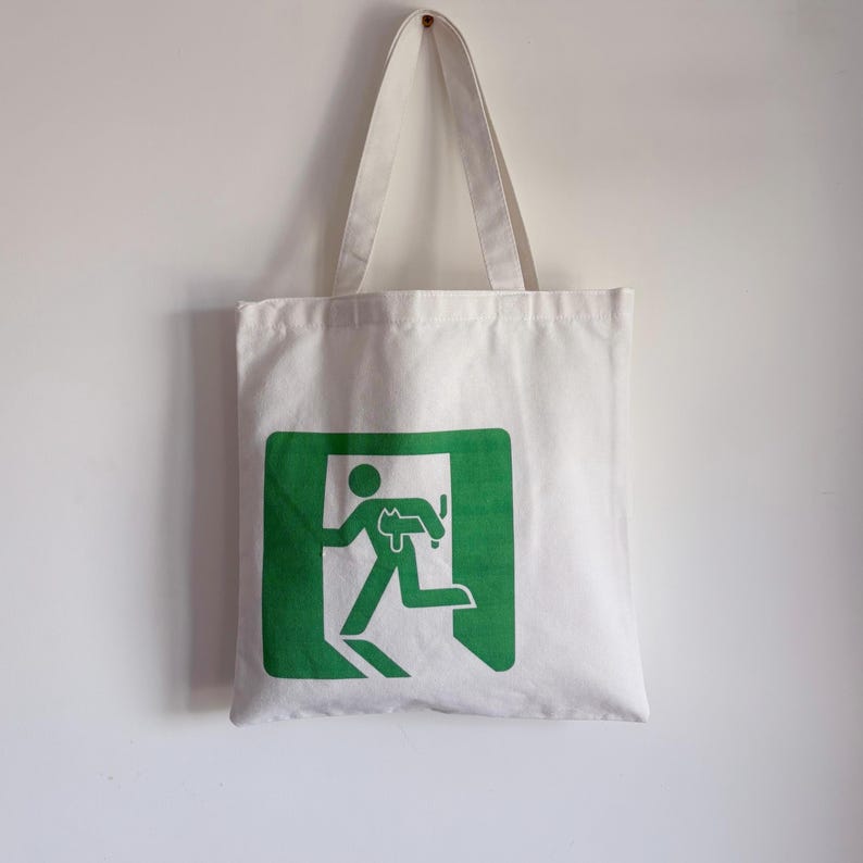 a white canvas tote bag with exit sign, little green person holding a cat to escape