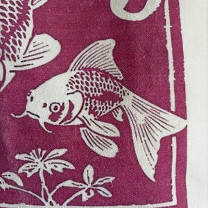 May include: A close-up of a fabric with a repeating pattern of white koi fish on a deep magenta background. The fish are detailed with scales and fins. The design includes stylized plants and a white border.