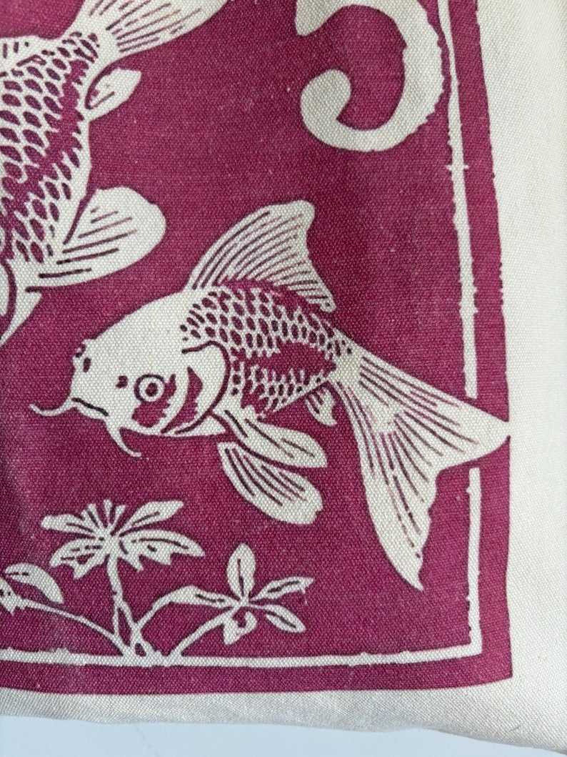 May include: A close-up of a fabric with a repeating pattern of white koi fish on a deep magenta background. The fish are detailed with scales and fins. The design includes stylized plants and a white border.