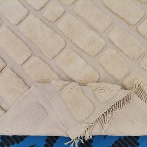 May include: A cream-colored rug with a brick pattern. The rug has a fringe border and is made of a soft, fluffy material.