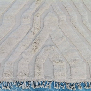 May include: A white, fluffy rug with a geometric pattern. The rug has a fringe border and is made of a soft, plush material.
