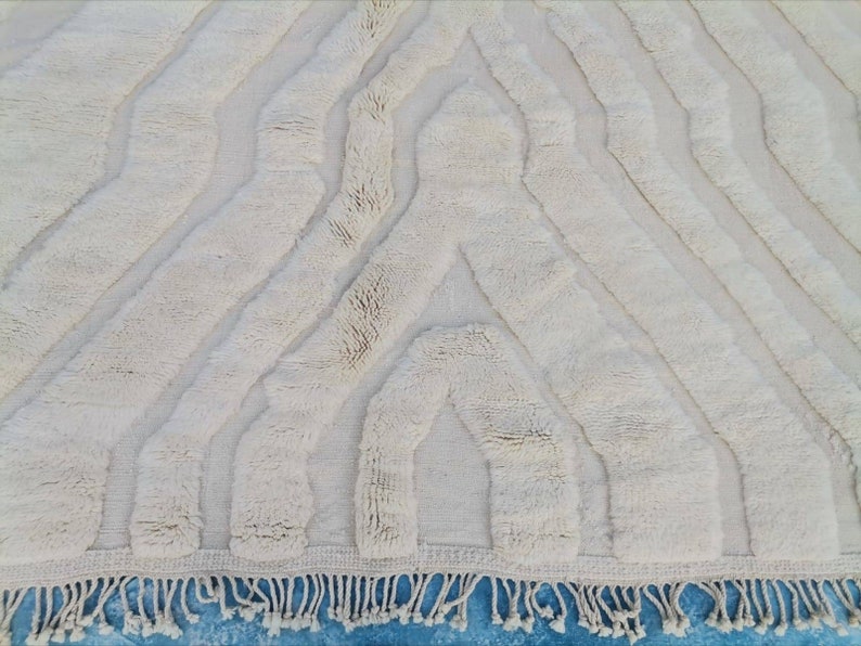 May include: A white, fluffy rug with a geometric pattern. The rug has a fringe border and is made of a soft, plush material.