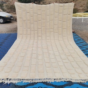 May include: A large, off-white, woven rug with a brick pattern. The rug is laid out on a blue and white patterned surface.
