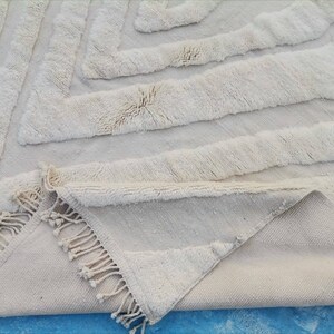 May include: A white, fluffy rug with a geometric pattern. The rug has a fringe border and is folded in half.