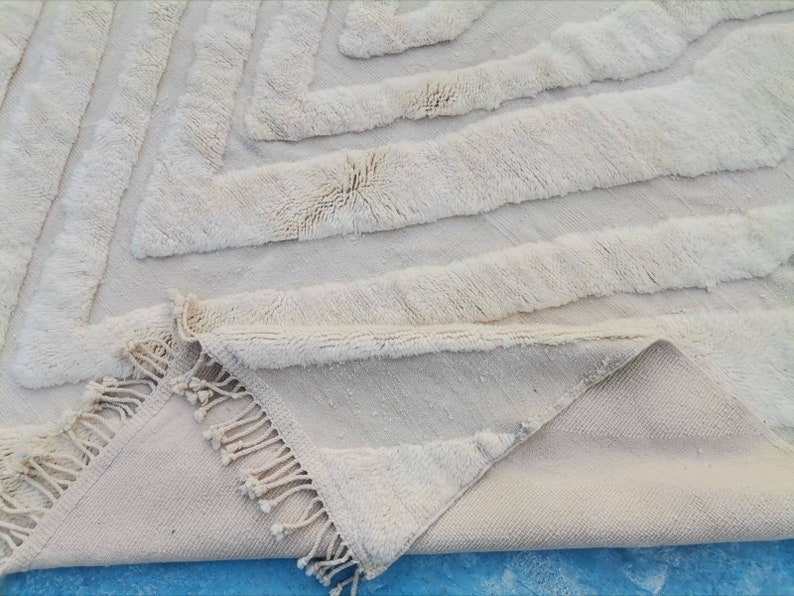 May include: A white, fluffy rug with a geometric pattern. The rug has a fringe border and is folded in half.