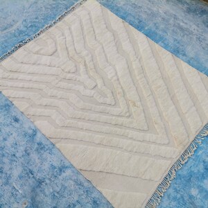 May include: A white, fluffy rug with a geometric pattern. The rug has a fringe border and is made of a soft, textured material.