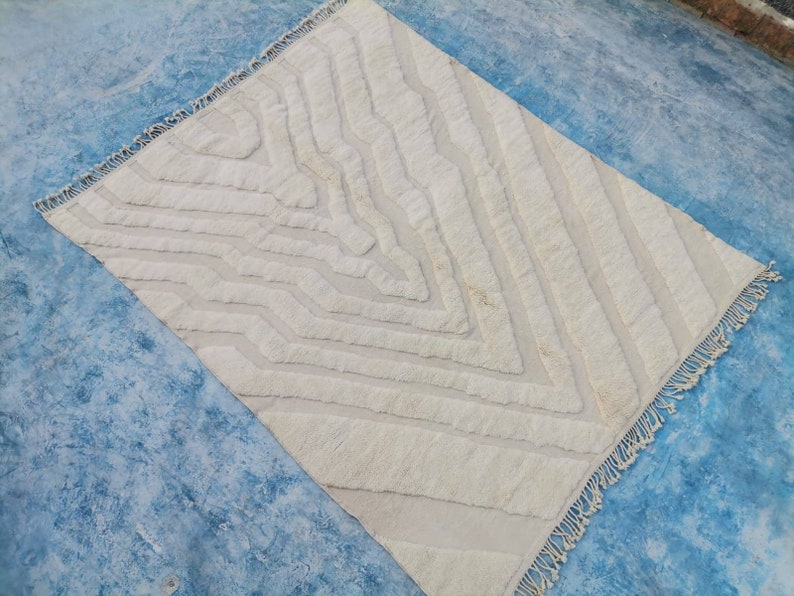 May include: A white, fluffy rug with a geometric pattern. The rug has a fringe border and is made of a soft, textured material.