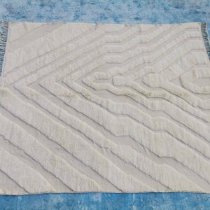 May include: A white, hand-woven rug with a geometric pattern. The rug has a fringe border and is made of natural fibers.