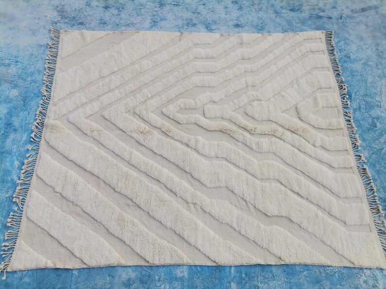 May include: A white, hand-woven rug with a geometric pattern. The rug has a fringe border and is made of natural fibers.