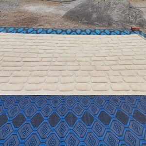 May include: A cream-colored rug with a textured, brick-like pattern. The rug is laid out on a blue and black patterned surface.