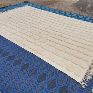 May include: A white rug with a textured brick pattern. The rug has a fringe border and is lying on a blue and black patterned rug.