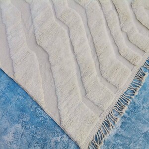 May include: A white, fluffy rug with a chevron pattern and fringe edging. The rug is laid out on a blue surface.