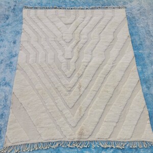 May include: A white, hand-woven rug with a geometric pattern. The rug has a fringe border and is made of natural fibers.