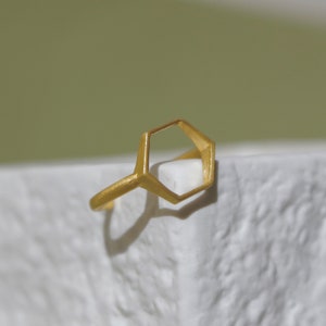 Può includere: Un anello d'oro a forma esagonale. L'anello è aperto e ha una finitura liscia e lucida.