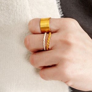May include: A set of three gold rings. The top ring is a wide band, the middle ring is a thin twisted band, and the bottom ring is a thin twisted band.