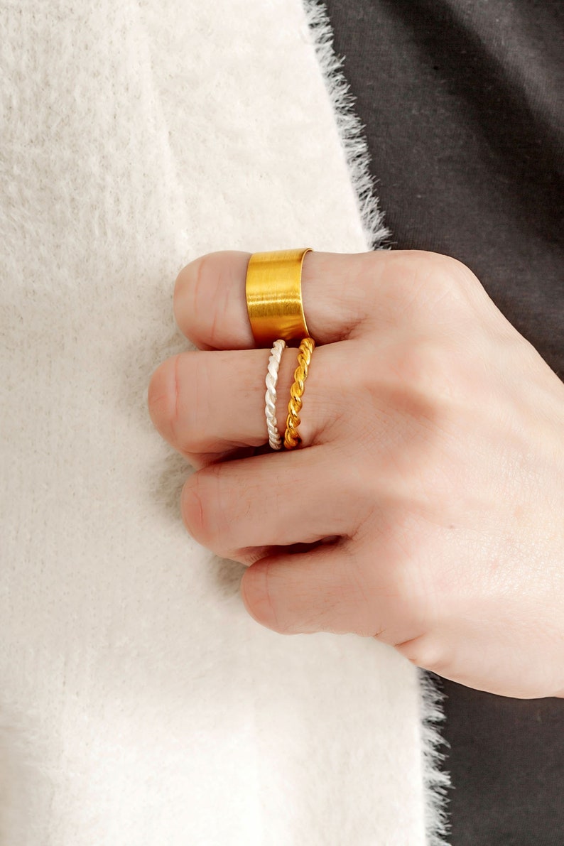 May include: A set of three gold rings. The top ring is a wide band, the middle ring is a thin twisted band, and the bottom ring is a thin twisted band.