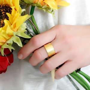 May include: A gold hammered ring on a finger holding a bouquet of yellow sunflowers and a red rose.