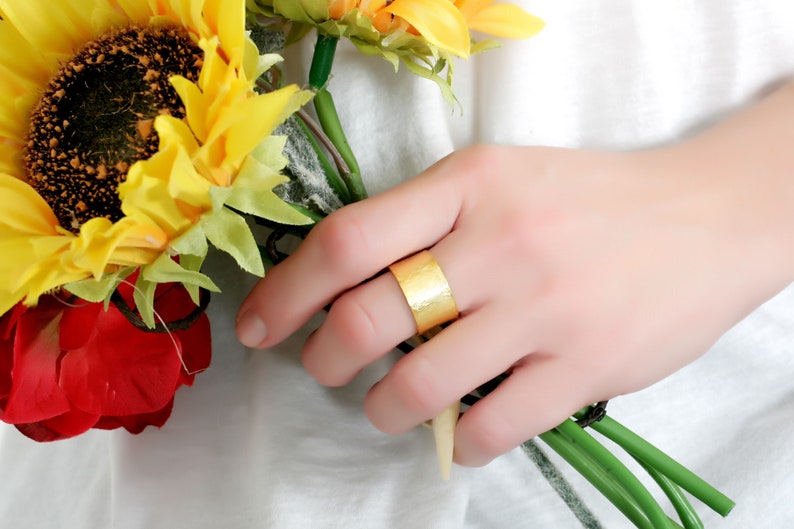 May include: A gold hammered ring on a finger holding a bouquet of yellow sunflowers and a red rose.