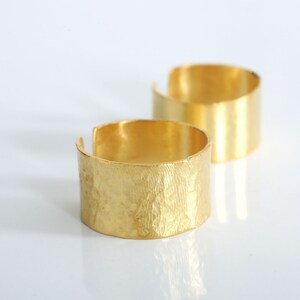 May include: Two gold-toned metal rings. The ring on the left has a textured surface. The ring on the right has a smooth surface.