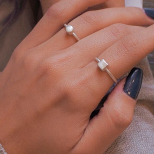 Può includere: Due anelli d'argento con forme geometriche. L'anello a sinistra ha una forma rotonda, e l'anello a destra ha una forma quadrata.