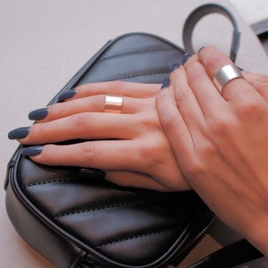 May include: Two hands wearing simple silver and gold band rings. The hands are resting on a black quilted purse.