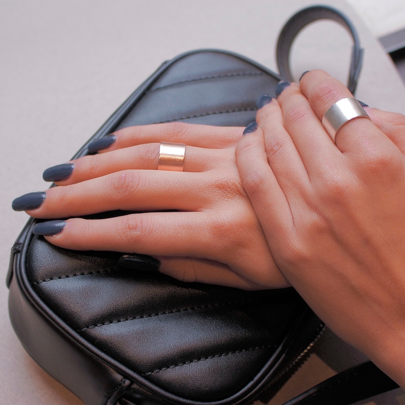 May include: Two hands wearing simple silver and gold band rings. The hands are resting on a black quilted purse.