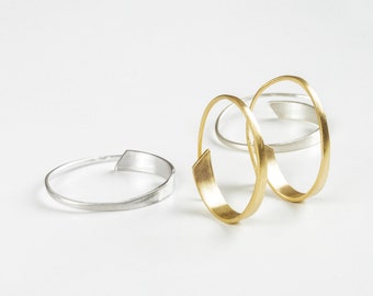 May include: Three simple, modern hoop earrings. Two are gold and one is silver.