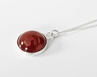 Puede incluir: Un collar de plata con un colgante redondo de piedra de cornalina roja.