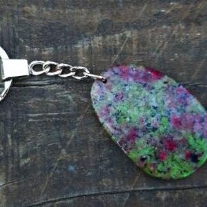 Puede incluir: Un llavero de piedra preciosa verde, rosa y negra con una cadena y un anillo de plata.