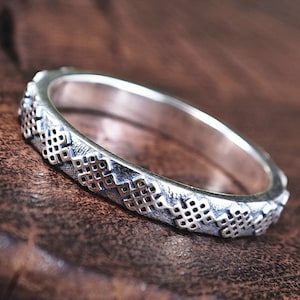 Puede incluir: Un anillo de plata con un diseño de nudo detallado. El anillo está sobre una superficie de madera.