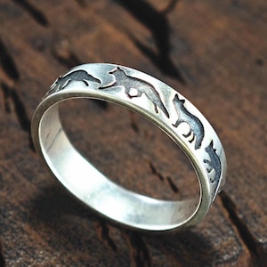 Puede incluir: Un anillo de plata con un diseño de varios animales corriendo alrededor de la banda. Los animales están en silueta y parecen ser lobos o perros.