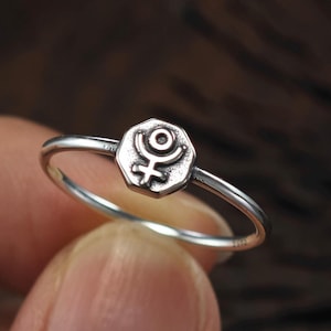 May include: A silver ring with a hexagonal shaped band featuring the astrological symbol for Uranus.