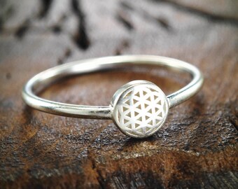 Op de afbeelding: Een zilveren ring met een rond, wit, geometrisch ontwerp. De ring ligt op een donkerbruin houten oppervlak.
