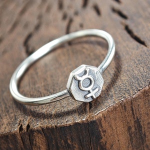 Op de afbeelding: Een zilveren ring met een zeshoekig ontwerp met het astrologische symbool voor Venus.