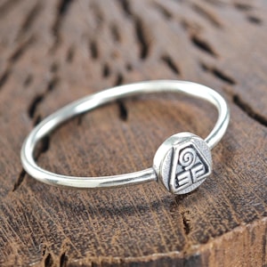 May include: A silver ring with a stylized symbol of four elements, representing earth, air, fire, and water. The ring is on a wooden surface.