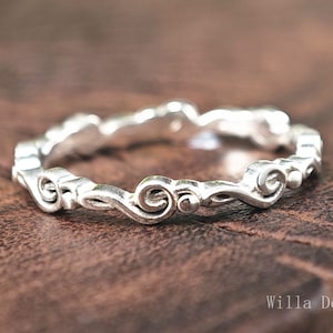 May include: A silver ring with a delicate, ornate design featuring swirls and curves. The ring is simple and elegant.