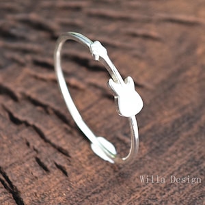 Op de afbeelding: Een zilveren ring met een gitaar silhouet ontwerp. De ring is open en heeft een eenvoudige, minimalistische stijl.