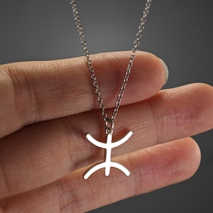 Peut inclure: Un collier en chaîne argent avec un pendentif en forme de silhouette humaine stylisée. Le pendentif est en argent et a une finition lisse et polie.