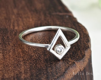 May include: A silver ring with a geometric diamond shape design featuring a small clear stone in the center.