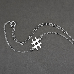 Puede incluir: Un brazalete de cadena de plata con un dije de hashtag de plata.