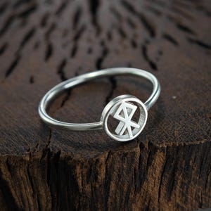 Könnte beinhalten: Ein silberner Ring mit einem runden Design, das ein nordisches Runensymbol zeigt. Der Ring liegt auf einer Holzoberfläche.