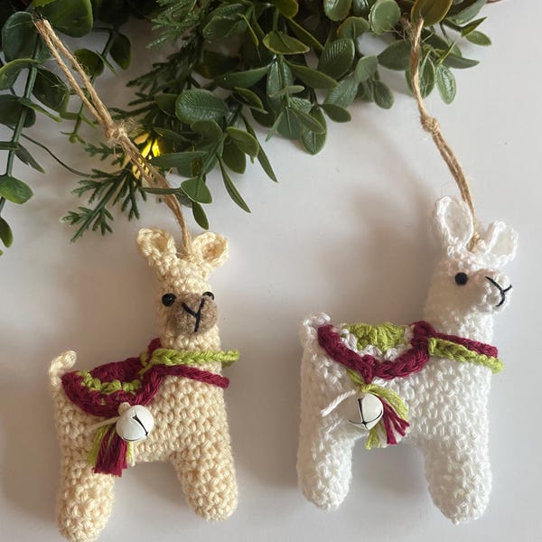 May include: Two handmade crochet llama ornaments. One is cream-colored with a brown muzzle and a burgundy and green scarf. The other is white with a burgundy and green scarf. Both have small silver bells and twine hangers.