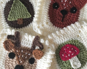 May include: A white crocheted blanket with various animal and nature motifs. The motifs include a deer, a mushroom, a tree, and a fox. The blanket is made with a soft, fluffy yarn.