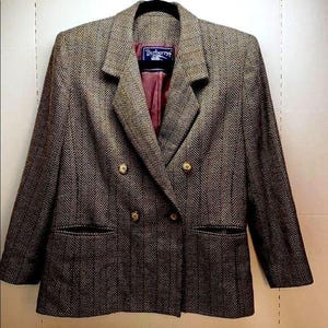 Pode incluir: Um blazer marrom e preto em espinha de peixe com fecho duplo e botões dourados. O blazer tem uma etiqueta que diz "Burberrys".