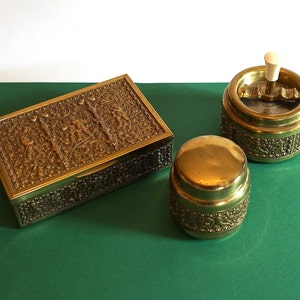 Può includere: Un set di tre scatole decorative in metallo dorato con intricati disegni floreali. Le scatole sono su una superficie verde.