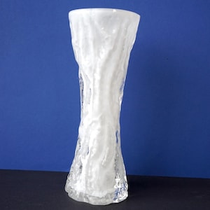 May include: A white glass vase with a textured surface. The vase is tall and slender, with a rounded base and a narrow opening.