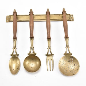 May include: Set of four brass kitchen utensils with wooden handles. The utensils include a spoon, a ladle, a fork, and a slotted spoon.