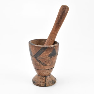 Könnte beinhalten: Ein Mörser und Stößel aus Holz mit geometrischem Muster. Der Mörser ist braun mit schwarzen Akzenten und der Stößel ist ein einfacher brauner Zylinder.