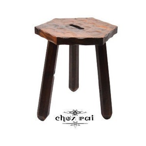 Può includere: Uno sgabello in legno rustico con piano esagonale e tre gambe. Lo sgabello è realizzato in legno marrone scuro e ha un aspetto naturale e non rifinito.